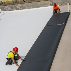 2 workers installing GAF TPO roofing system onto commercial rooftop