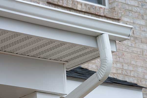 White k-style gutter system with a downspout, attached to the fascia of a home
